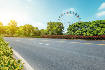 Asphalt road and ferris wheel playgrounds with green tree in the city park