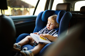 Little boy sitting in the car seat in the car, holding a book.