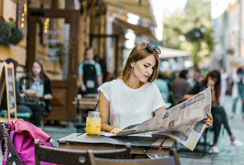 Plakat Ładnego uczciwego włosy caucasian turystyczna dziewczyna z okularami przeciwsłonecznymi na jej głowie ma przerwę z lemonad napojem i miasto mapą w ulicznej kawiarni, słoneczny dzień