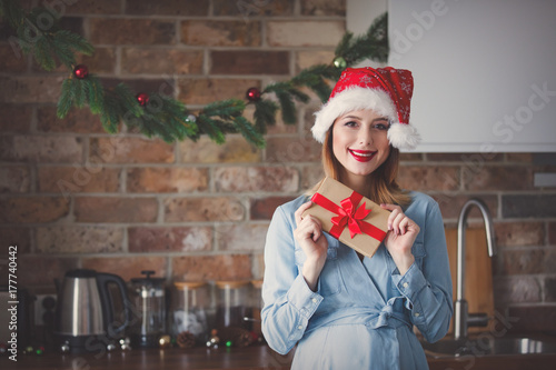 Plakat kobieta w kapeluszu Świętego Mikołaja w kuchni z prezentami