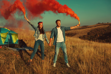 Wall Mural - Young happy couple holding smoke bombs on camping