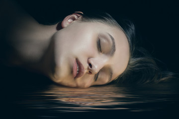 Wall Mural - beautiful female head with closed eyes lying on water with reflections