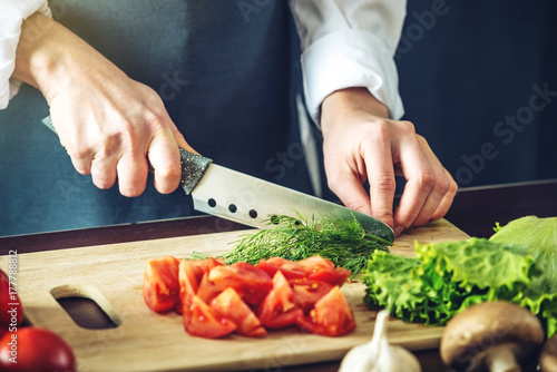 Zdjęcie XXL Szef kuchni w czarnym fartuchu tnie warzywa. Koncepcja ekologicznych produktów do gotowania