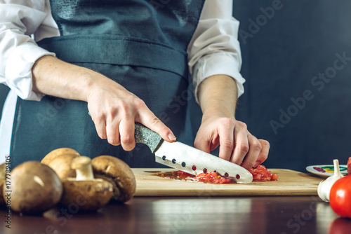 Zdjęcie XXL Szef kuchni w czarnym fartuchu pokroił pomidory. Koncepcja ekologicznych produktów do gotowania