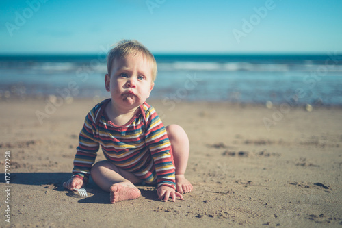 Plakat Mały chłopiec siedzi na plaży