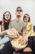 © proimagecontent - Group of teen friends having fun watching the 3D film with glasses while eating popcorn on grey sofa
