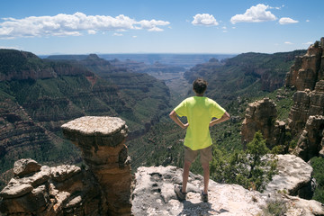 A teenager stands on the edge of a rock and looks into the distance. North Rim Grand Canyon National Park Arizona, US