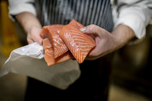 Close Up Of A Fish Monger’s Hands Holding Three Fillets Of Fresh Filleted Salmon On A Market Stall In Yorkshire, England, UK