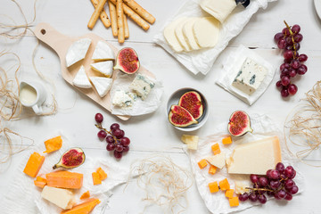 Various types of cheese with fruits and snacks on the wooden white table. Top view