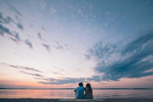 Young Man And Woman Sitting On Beach On Sunset