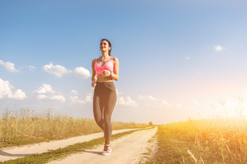 The woman running on the dirt road on the sunny background