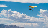 Orange and yellow hang glider in blue sky with clouds