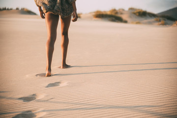 Legs of a young black woman walking in the sand in a desert dunes