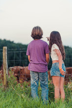 A Boy And A Girl Standing At A Fence Looking At Scottish Highlander Cows