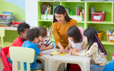 asian female teacher teaching mixed race kids reading book in classroom,kindergarten pre school conc