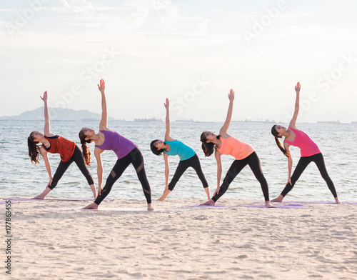 Fotografie, Obraz Yoga class at sea beach in evening ,Group of people doing Triangle poses with clam relax emotion at beach,Meditation pose,Wellness and Healthy balance lifestyle