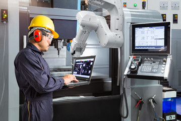 Maintenance engineer using laptop computer control automatic robotic hand with CNC machine in smart factory. Industry 4.0 concept