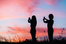 Silhouette Of Boy And Girl Photographing The Sunset With Their Mobile Phone