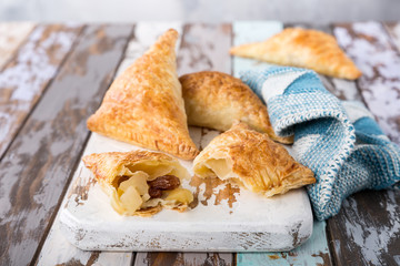 Puff pastry triangles filled with apples, dutch appelflappen on old cutting board. Homemade food concept with copy space.