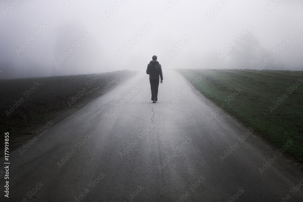 Man walking alone on rural misty asphalt road - obrazy, fototapety, plakaty 
