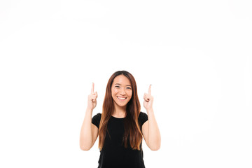 Wall Mural - Young cheerful asian girl in black tshirt  pointing with two fingers upward, looking at camera