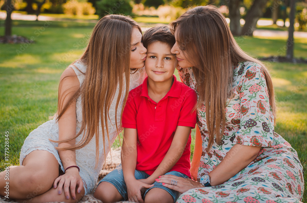 Happy mother, son and daughter in the park. Mom and sister kiss their