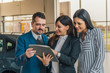 © bnenin - Shot of a handsome salesman showing documents to his happy clients at the dealership.