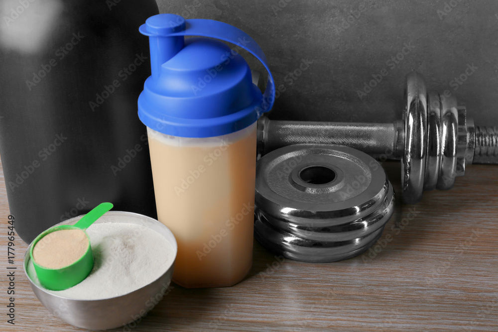 Composition with protein shake, powder and dumbbell on table