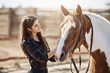 © Liubov Levytska - Young female barn manager taking care and talking to a young stallion preparing for a ride.