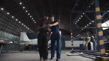 Two Flight Engineers Walking Through A Large Aircraft Hangar Talking And Gesturing Together