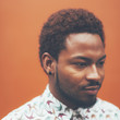 © BONNINSTUDIO/Stocksy - Square portrait of modern young black man in front a orange wall.