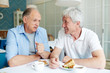 © pressmaster - Communication of two friendly senior men by cup of tea and dessert in cafe