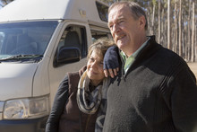 Frontal View Of Grey Nomad Couple Standing In Front Of Parked Campervan