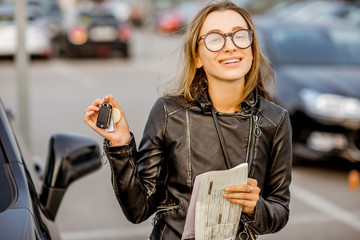 Wall Mural - Portrait of a young happy woman with keys and rental contract standing near the car on the outdoor parking