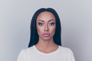 Close up portrait of young brunette afro lady with serious grimace, on pure grey backgrund and looking in the camera, She is in a casual white outfit, with cosmetics