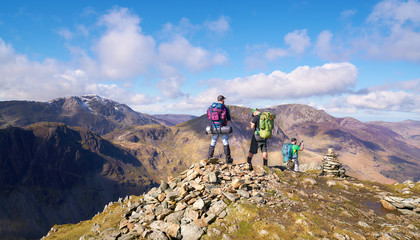 Three hikers looking out over the summits of High Crag, High Stile and Pillar from the summit of Fleetwith Pike, English Lake District.