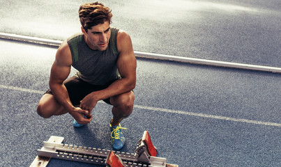 Wall Mural - sprinter sitting beside a starting block on running track
