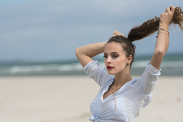 Wall Mural - Young cute woman wear tied shirt on the beach fixing her ponytail