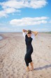© raisondtre - Beautiful elegant girl in black dress and white jacket is on the sandy beach, barefoot, his hands behind his head