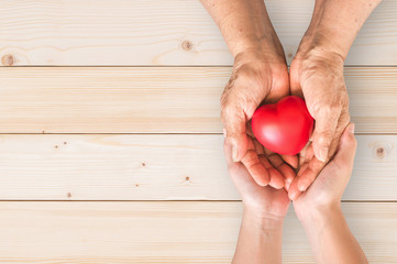Wall Mural - Elderly senior person or grandparent's hands with red heart  in support of nursing family caregiver for national hospice palliative care and family caregivers month concept