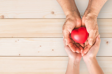 Elderly senior person or grandparent's hands with red heart  in support of nursing family caregiver for national hospice palliative care and family caregivers month concept