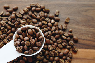 dark roasted specialty coffee beans in the white plastic spoon on wooden background ready to make a cup of coffee.