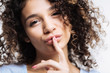 Curly-haired woman pouting and pressing finger to lips