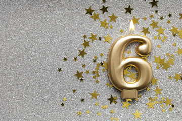 Number 6 gold celebration candle on star and glitter background