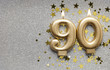 Number 90 gold celebration candle on star and glitter background