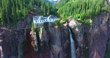 Aerial View Of House On Cliff By Horsetail Waterfall With Green Pine Forest Background - Bridal Veil Falls, Colorado, USA