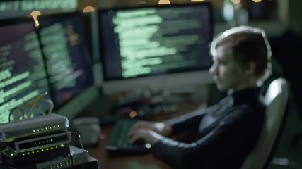 Cinemagraph of woman typing programming code on multiple screen computers in dark office at night; green data running on displays
