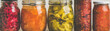 Autumn seasonal pickled or fermented vegetables in jars placed in row over vintage kitchen drawer, white wall background, close-up. Fall home food preserving or canning