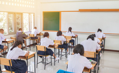 Behind girls group undergraduate students testing of examination in room and student sitting on row chair doing final exams in classroom with Thailand uniform. Asian Education Concept.