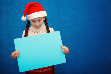 Little girl in Santa hat holding blank sheet of paper